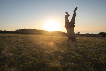 Young muscular man practicing hand stand during a magical sunset. Asturias, Spain.