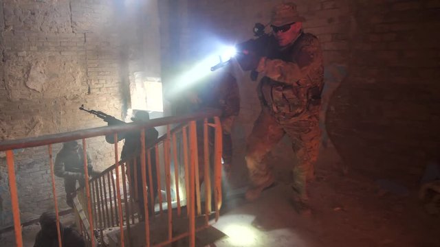 Group of special forces fighters in camouflage with weapons and tactical devices investigating enemy territory during hostage rescue operation. Warriors moving in short dashes through ruined building
