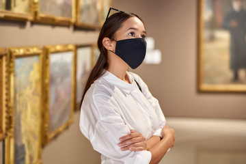 Woman visitor wearing an antivirus mask in museum looking at pictures.
