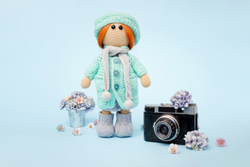 Knitted interior amigurumi doll in winter clothes with a flower composition and vintage camera on a...