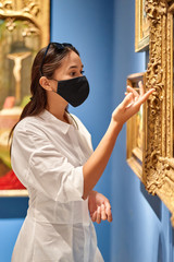 Girl visitor wearing an antivirus mask standing near pictures in museum.