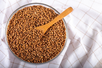Bowl of raw buckwheat with spoon on wooden background. Buckwheat groats (hulled seeds) in bowl.