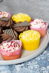 Variety of cupcakes on a grey plate.  Blue patterned tile background