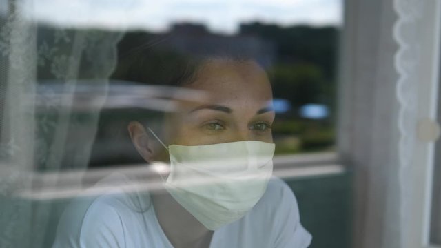 Young woman wears a mask to protect herself from covid-19 while looking out the window