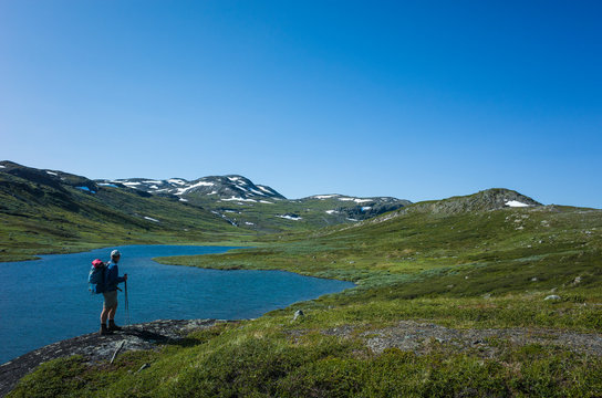 Hiking in Swedish Lapland. Man traveler trekking alone with view of mountain lake Allagasjavri in Sweden. Arctic nature of Scandinavia in warm summer sunny day with blue sky