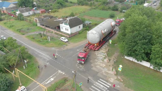 A truck driver with an oversized cargo on a trailer makes a turn on a narrow road, filmed from a drone, side view. Delivery and logistics of goods from different places, top view
