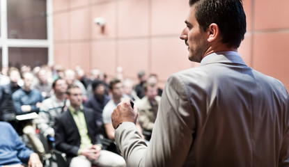 Speaker giving a talk on corporate business conference. Unrecognizable people in audience at...