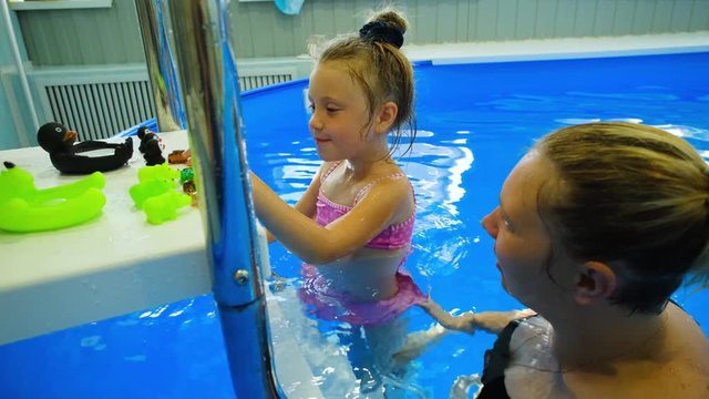 happy caucasian girl 5-6 years old learns to swim in the pool with a coach. Mother trains daughter in the water.