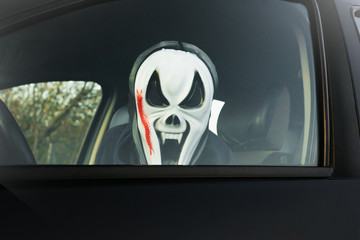 Halloween. Man in a terrible mask in a car in the driver's seat harvests pumpkins and scares.