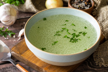 Hot rich meat broth (bouillon) with herbs on a rustic table.