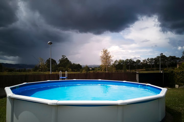 sunlit swimming pool on stormy day with dark clouds , bad omen concept