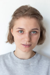 portrait of caucasian woman with clean skin, short hair posing in gray sweatshirt on white background, looking at camera. model tests of pretty girl in basic clothes, close up. attractive female poses