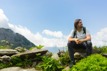 Naklejka na ściany i meble Young hiker sit in beautiful mountains on hiking trip. Active person resting outdoors in nature. Backpacker camping outside recreation active
