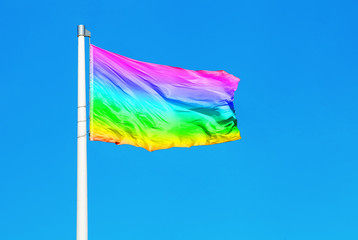 Rainbow flag waving on the wind against clear blue sky
