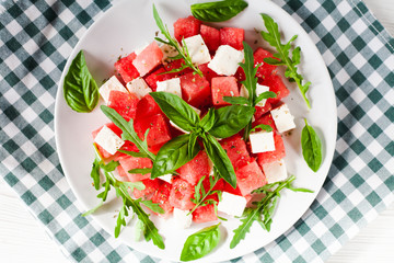 Delicious fresh salad with watermelon, feta cheese, arugula and basil leaves on white plate. Close-up. Top view. Healthy food concept.