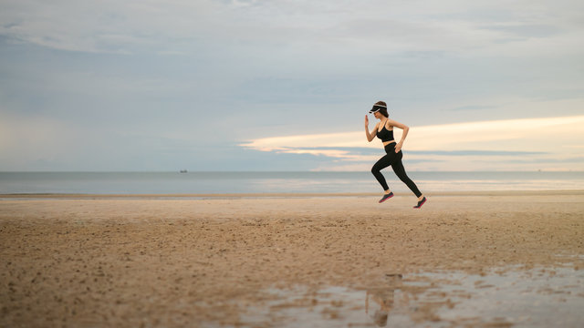 Side view of young woman in sportswear jogging on beach in the morning.