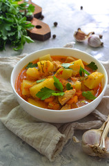 Vegetable stew in a white bowl. Light background. Linen cloth. Stew with potatoes, chicken, carrots and herbs. Vertical view