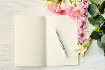 Notebook with pen and flowers on white wooden background