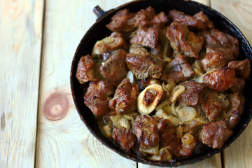 Selective focus. Fried meat pieces in a frying pan. Appetizing grilled meat with onions. Cooked pork.