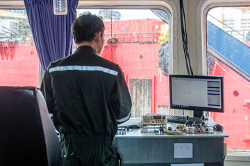 A captain looking into navigation screen at stern control panel of a tug boat while on the job at...