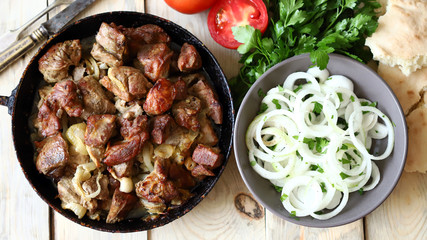 Selective focus. Fried meat pieces in a frying pan. Appetizing grilled meat with onions. Cooked pork.