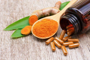 Tumeric powder capsules, Turmeric root ( curcumin, Curcuma ) with green leaf isolated on wood table background. 