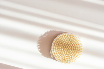 Dry massage brush made of natural materials on a light pastel background. Beautiful solar chiaroscuro. Minimalism, copy space.