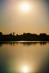 Vertical photo of sunset landscape with sun reflection in river