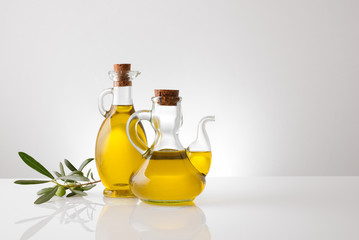 Containers with oil and olive twig on white table front
