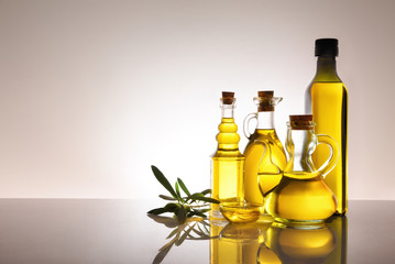 Four assorted glass containers with olive oil backlit on table
