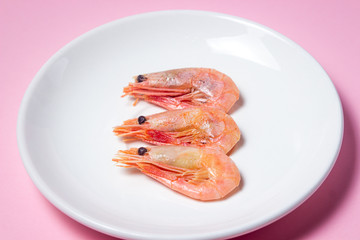 Shrimps on a white plate. Boiled shrimp in a plate on a pink background. Three shrimps lie next to each other