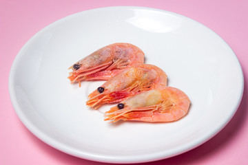 Shrimps on a white plate. Boiled shrimp in a plate on a pink background. Three shrimps lie next to each other