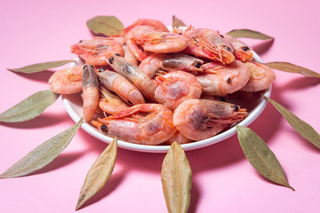 Shrimps on a white plate. Boiled shrimp in a plate on a pink background. Laurel leaves lie around