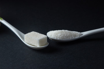 Sugar on a black background. Sugar cubes and granulated sugar. Sugar spoons