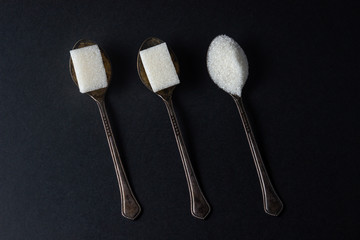Sugar on a black background. Sugar cubes and granulated sugar. Sugar spoons