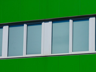 closeup of bright green color metal exterior siding of office building with white plastic strip...