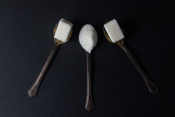 Sugar on a black background. Sugar cubes and granulated sugar. Sugar spoons