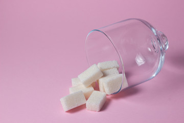 Sugar cubes on a pink background. Sugarcubes spilled out of glassware
