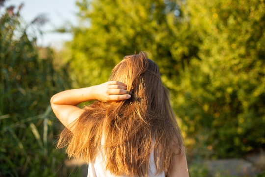 Blonde Woman With Long Hair Walking At A Park On A Sunny Day, Viewed From Behind