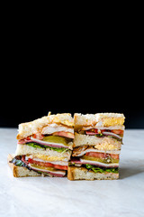 Classic Club Sandwich on Marble Surface. Includes Ham, Cheese, Lettuce, Tomato Slices. Light background. Close-up.