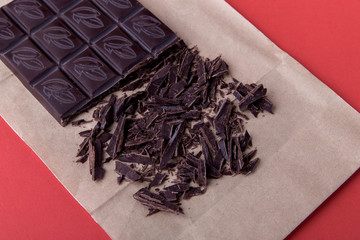 A bar of dark chocolate on a red background, next to large chocolate chips