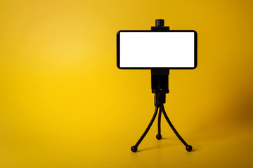 mobile phone mounted on mini tripod with blank screen isolated on yellow background. copy space