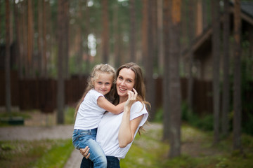 Fototapeta premium Happy smiling mother and her cute emotional little daughter child in white shirts and denim jeans are hugging and having fun outdoor in nature at countryside. Spending summer time with family.