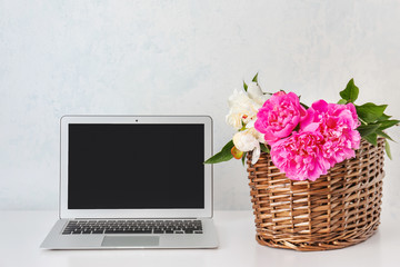 Table with laptop and peony flowers near light wall