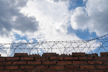 brick wall with barbed wire, with blue sky on background