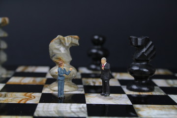 kleine Figuren von Geschäftsleuten auf einem Schachbrett mit Schachfiguren im Hintergrund 