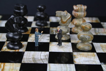 kleine Figuren von Geschäftsleuten auf einem Schachbrett mit Schachfiguren im Hintergrund  © johannes81