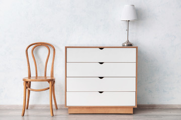 Modern chest of drawers with chair and lamp near light wall in room