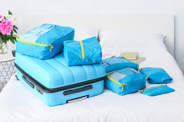 Suitcase and set of travel organizers with belongings on bed at home