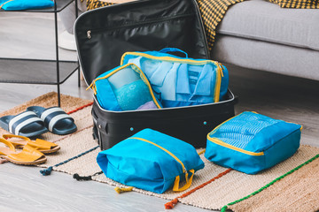 Suitcase and set of travel organizers with belongings at home